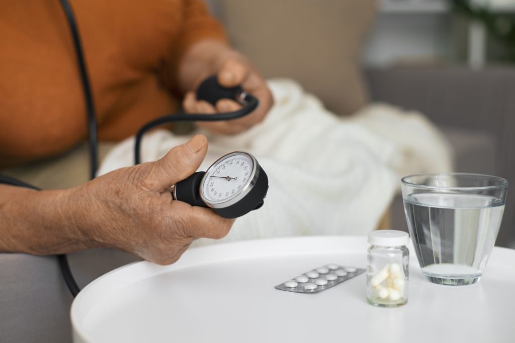 An elderly woman sits on a couch, using a blood pressure monitor, guided by a blood pressure specialist doctor.jpg