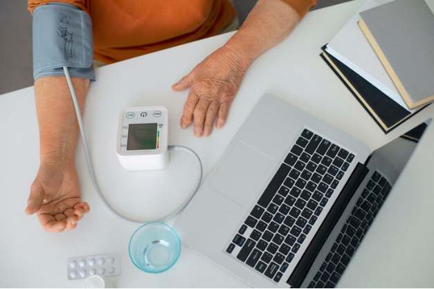 A person measures their blood pressure using a monitor, with a medical setting in the background.